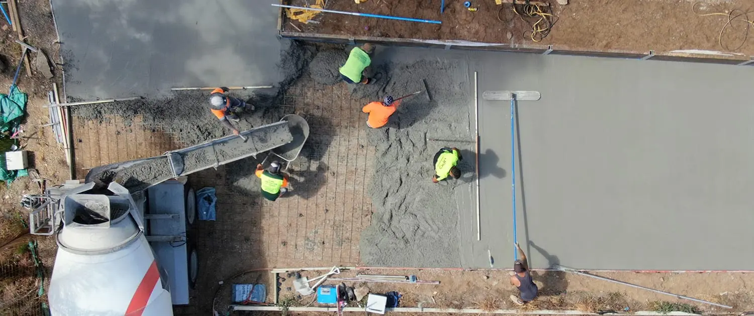 Overhead view of a concreting crew screeding and floating a fresh slab while the truck chute pours