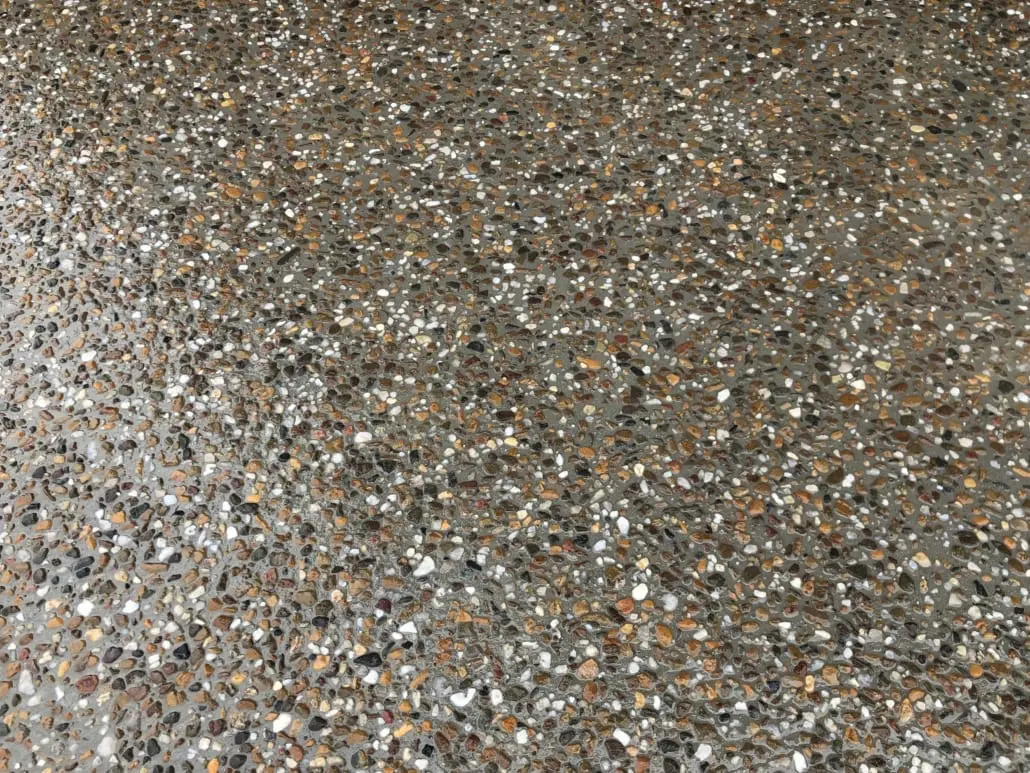 Close-up of exposed aggregate concrete showing honey, cream and dark brown river pebbles in a grey cement matrix