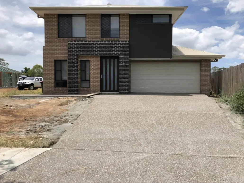 Exposed aggregate concrete driveway at a new brick home, honey and grey stone washed back