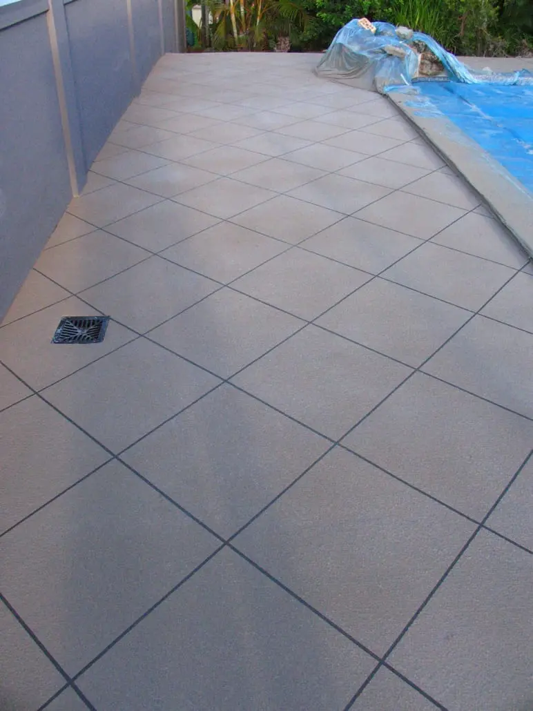 Charcoal concrete footpath with crossed white diamond banding running between garden beds