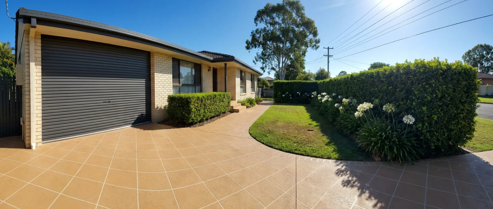 Sandstone-tan decorative concrete running continuously from driveway to curved path to front steps at a cream brick Brisbane home