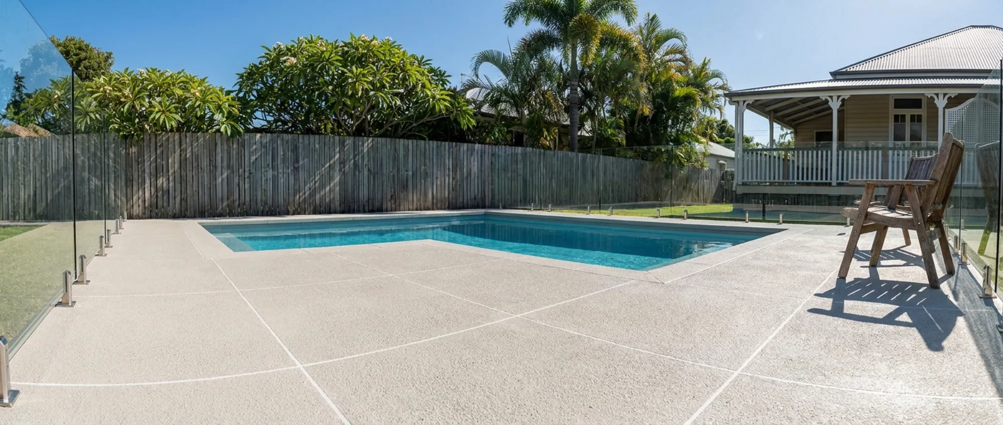 Pale sandy-grey non-slip decorative concrete pool surround with white grout lines beside a backyard pool