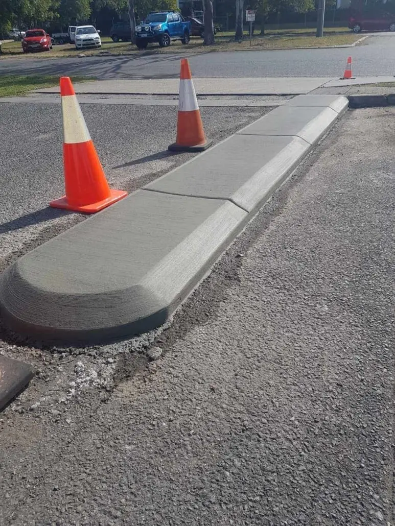 Freshly poured grey concrete kerbing and traffic island against asphalt, witches hats in place