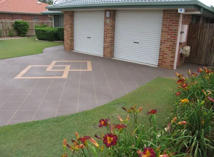 Grey decorative concrete driveway with a tan geometric border motif, running up to a double garage on a Brisbane brick home