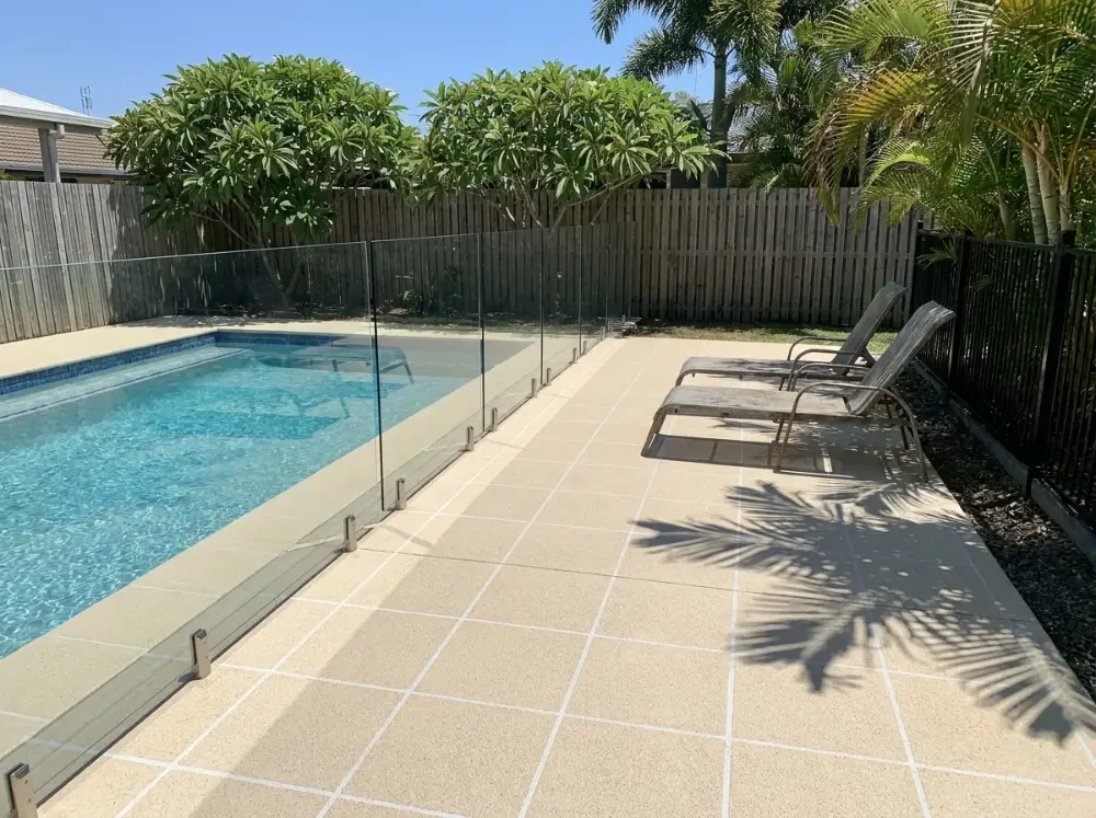 Pale sand-coloured non-slip decorative concrete pool surround with white grout and glass fencing