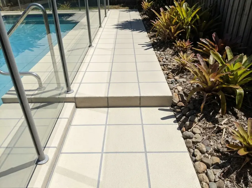 Cream square-tile non-slip concrete poolside path with two shallow steps and a handrail