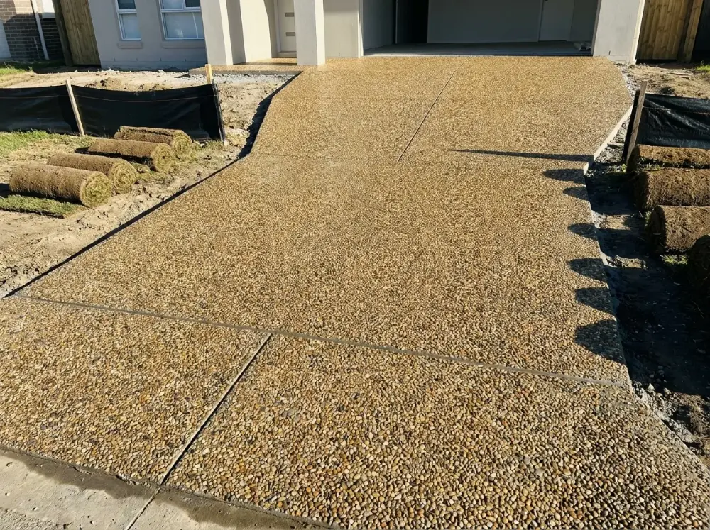 Newly poured exposed aggregate driveway of honey and brown river pebbles at a new-build home