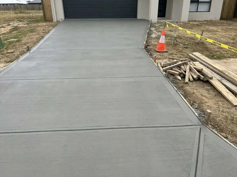 Freshly finished plain grey broom-finish concrete driveway with tooled edges and saw-cut joints