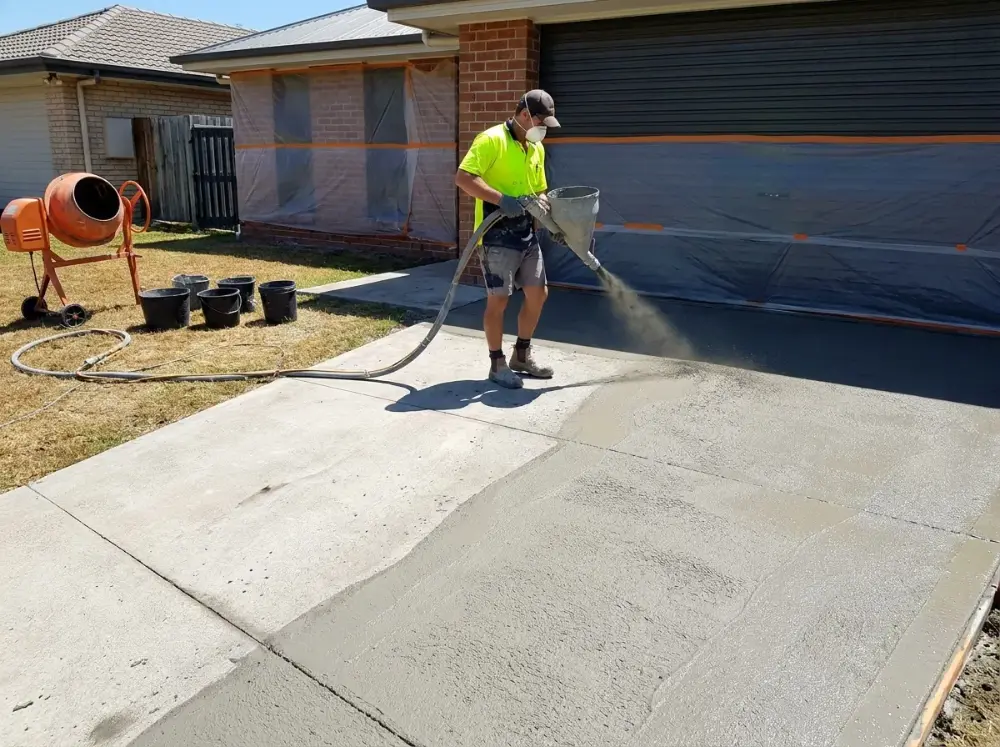 Concreter spraying a cementitious base coat over a masked-off driveway with a hopper gun