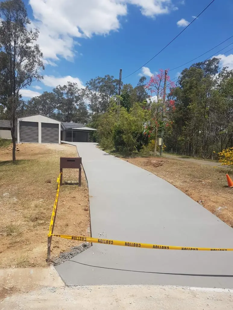 Long plain grey broom-finish concrete driveway leading to a Colorbond double garage