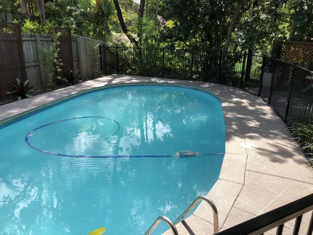 Grey speckled concrete pool surround cut into a square tile grid with dark grout, beside a blue pool