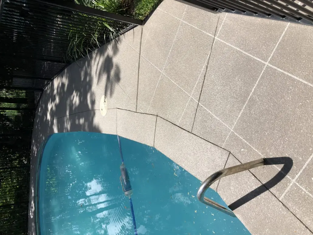 Speckled grey resurfaced concrete pool surround with fine joint lines around a backyard pool