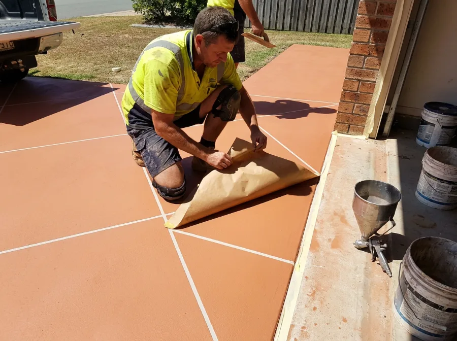 Concrete resurfacer kneeling on a fresh terracotta overlay, peeling back the stencil to reveal white grout lines